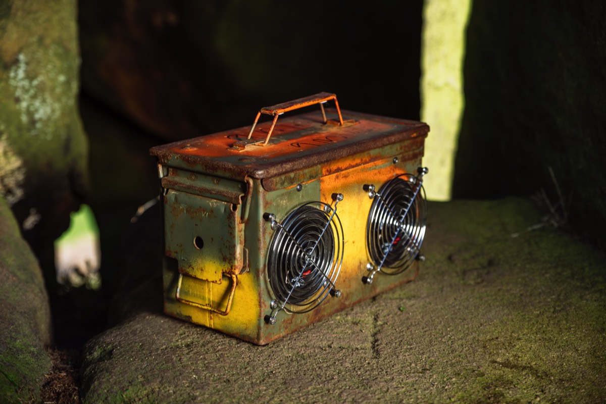 A patina-style rustic ammo box speaker on some rocks
